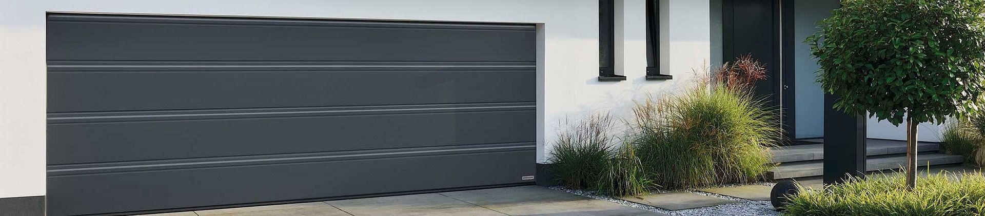 Modernes, graues Garagentor mit horizontalen Linien vor einem Haus mit Bepflanzung